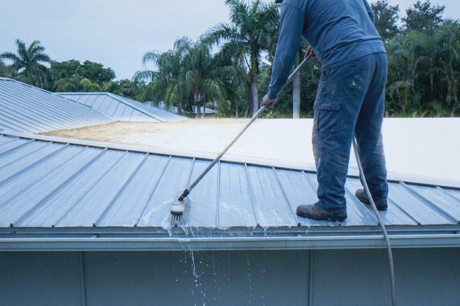Worker cleaning a standing seam metal roof with a soft-bristle brush and low-pressure water