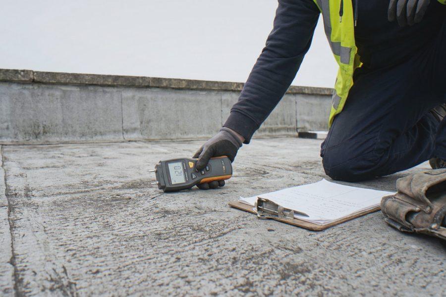 Roofer taking a moisture meter reading on an existing commercial flat roof before a re-cover quote
